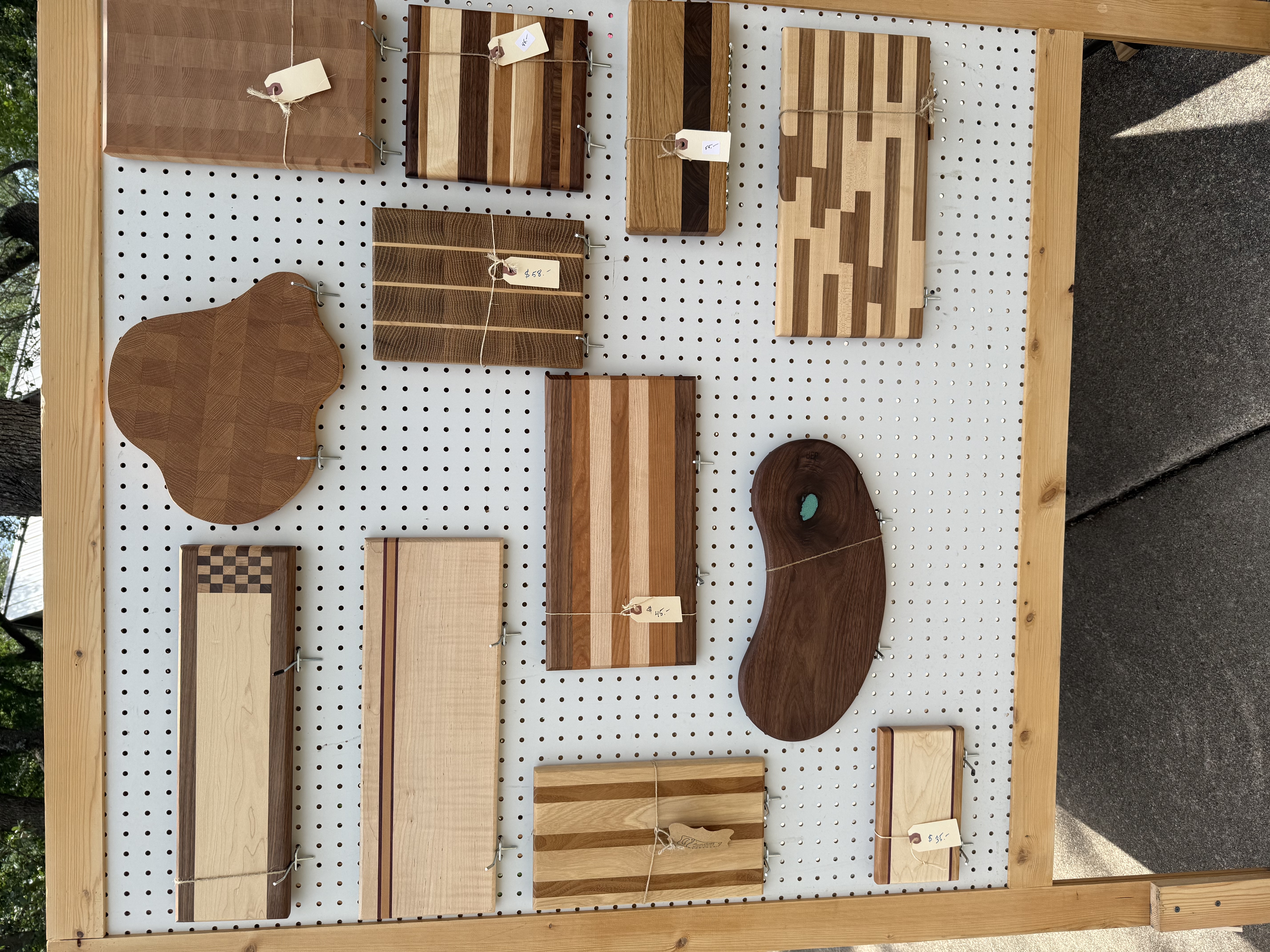 Outdoor pegboard display of cutting boards in many shapes and grain patterns