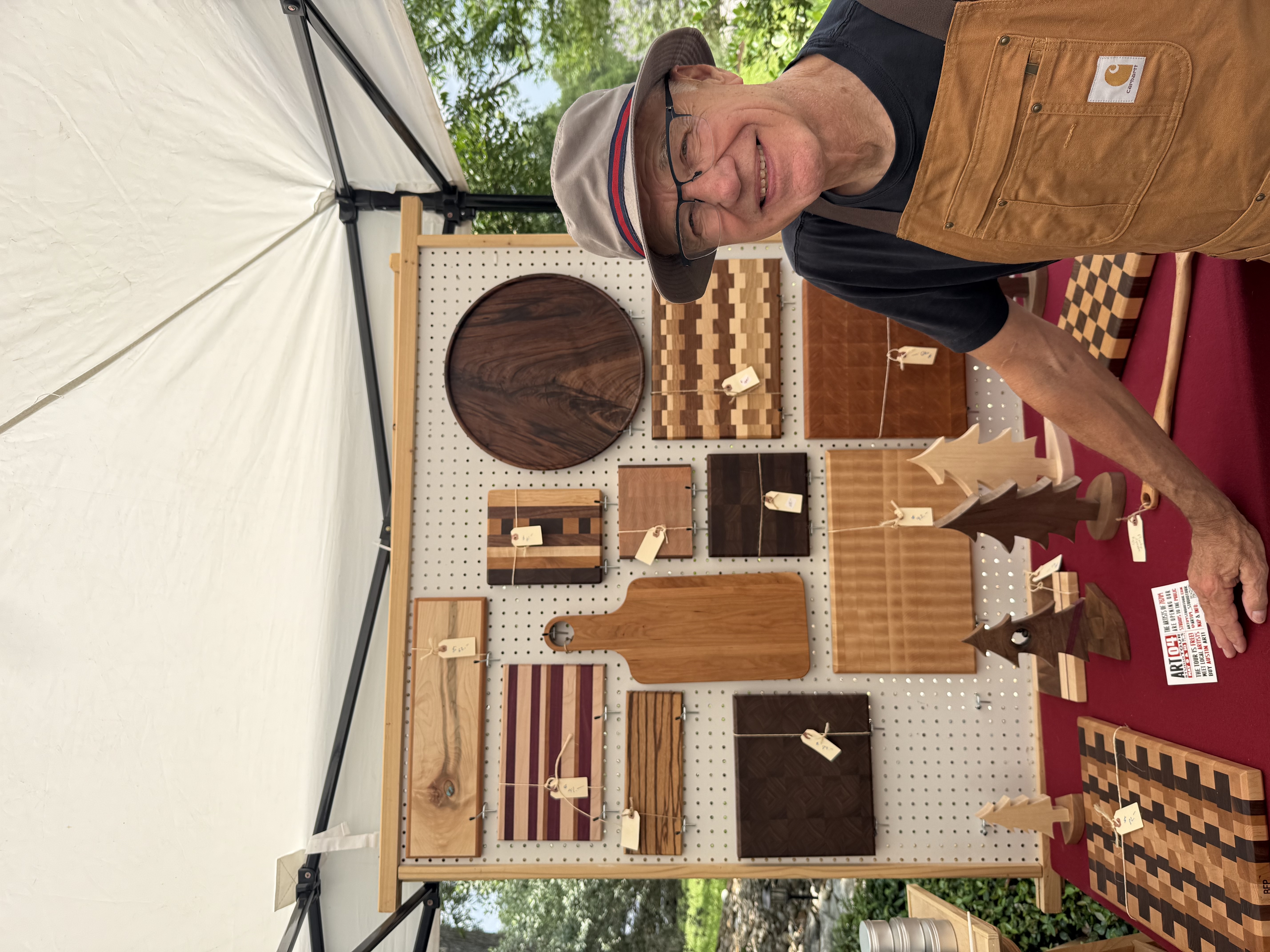 Buzz Pruitt smiling at his craft show booth, surrounded by his cutting boards